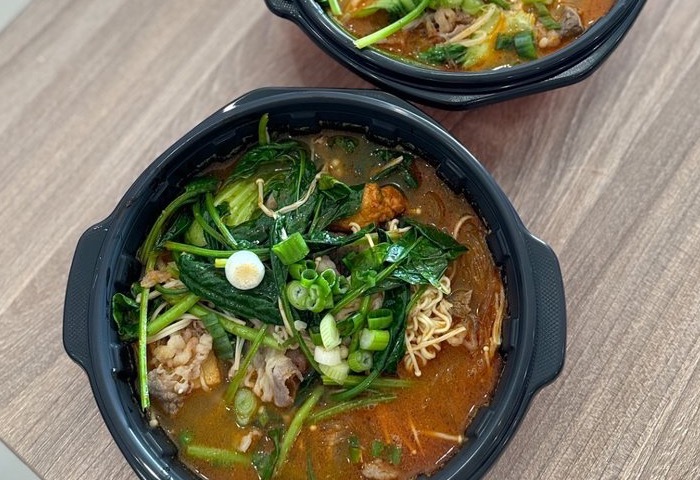 A freshly made bowl of X-Malatang topped with leafy greens, scallions, noodles, and beef in a spicy broth